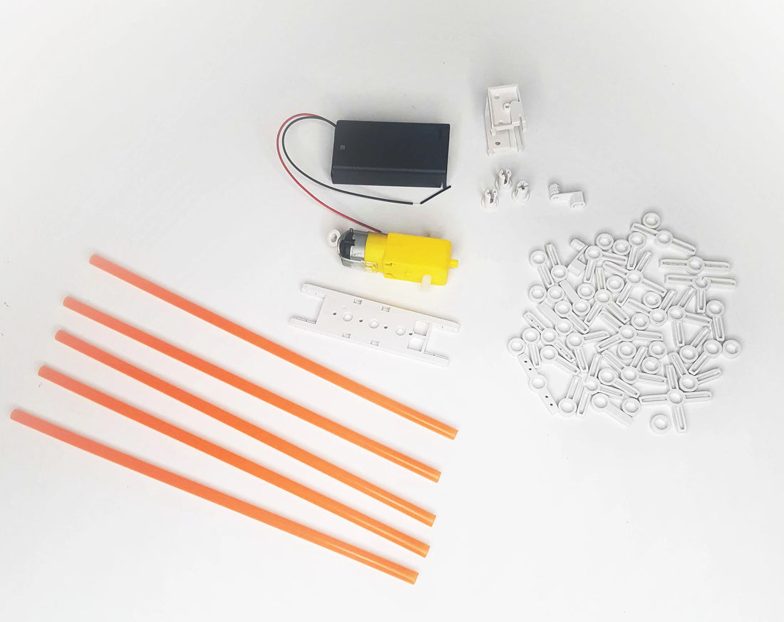 layout of orange straws, white plastic connectors, dc motor, AA battery case on white background